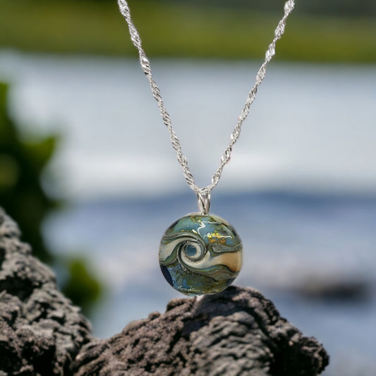 JSK Bluegreen Tidal Wave Lampwork Pendant&nbsp; By Glass Artist June Knowles.  Blues and greens with silver foil make this bead a statement piece.  The wave swirl adds movement and depth.  Sterling silver bail and chain.  18 inch chain and a 1.25 inch bead.  