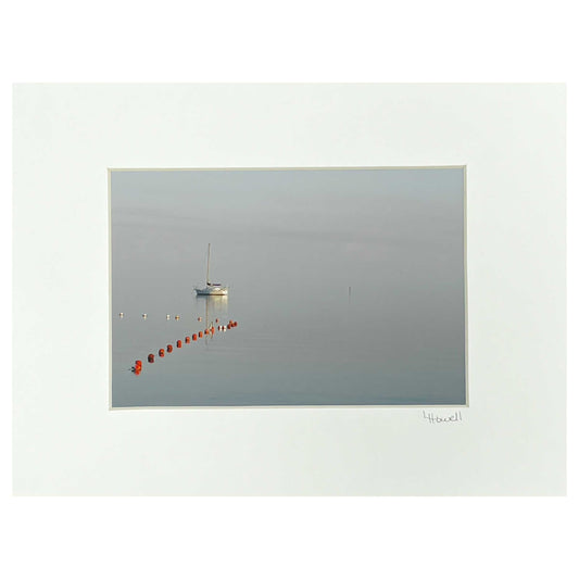 Single sail boat flowing in the water in the left hand side of the frame with red buoys in front of it. In a white mat.  signed by the Photographer.
