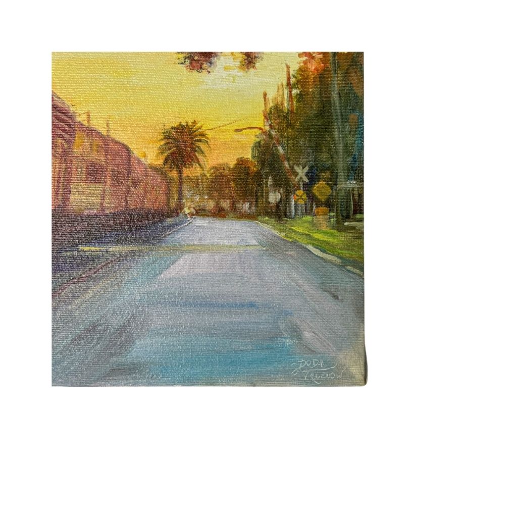 Close up view of roadway. Sunset Train. Full view of canvas with road and trees and railroad crossing next to the train on the tracks.l Painting of an old train at sunset. Sky is yellow, train is blue and yellow with red on the cars.